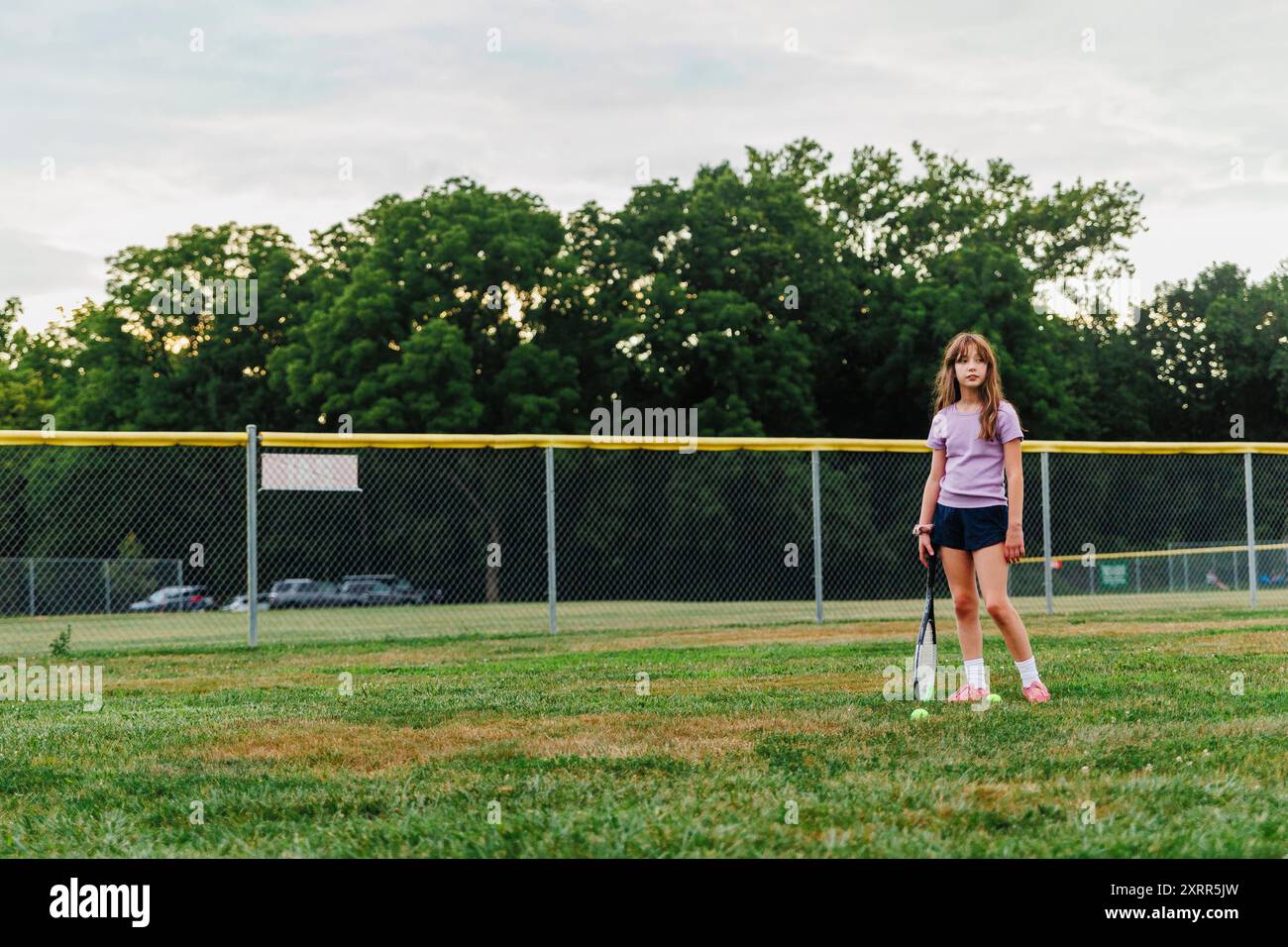Ein ernstes Mädchen steht mit Tennisschläger im Feld Stockfoto