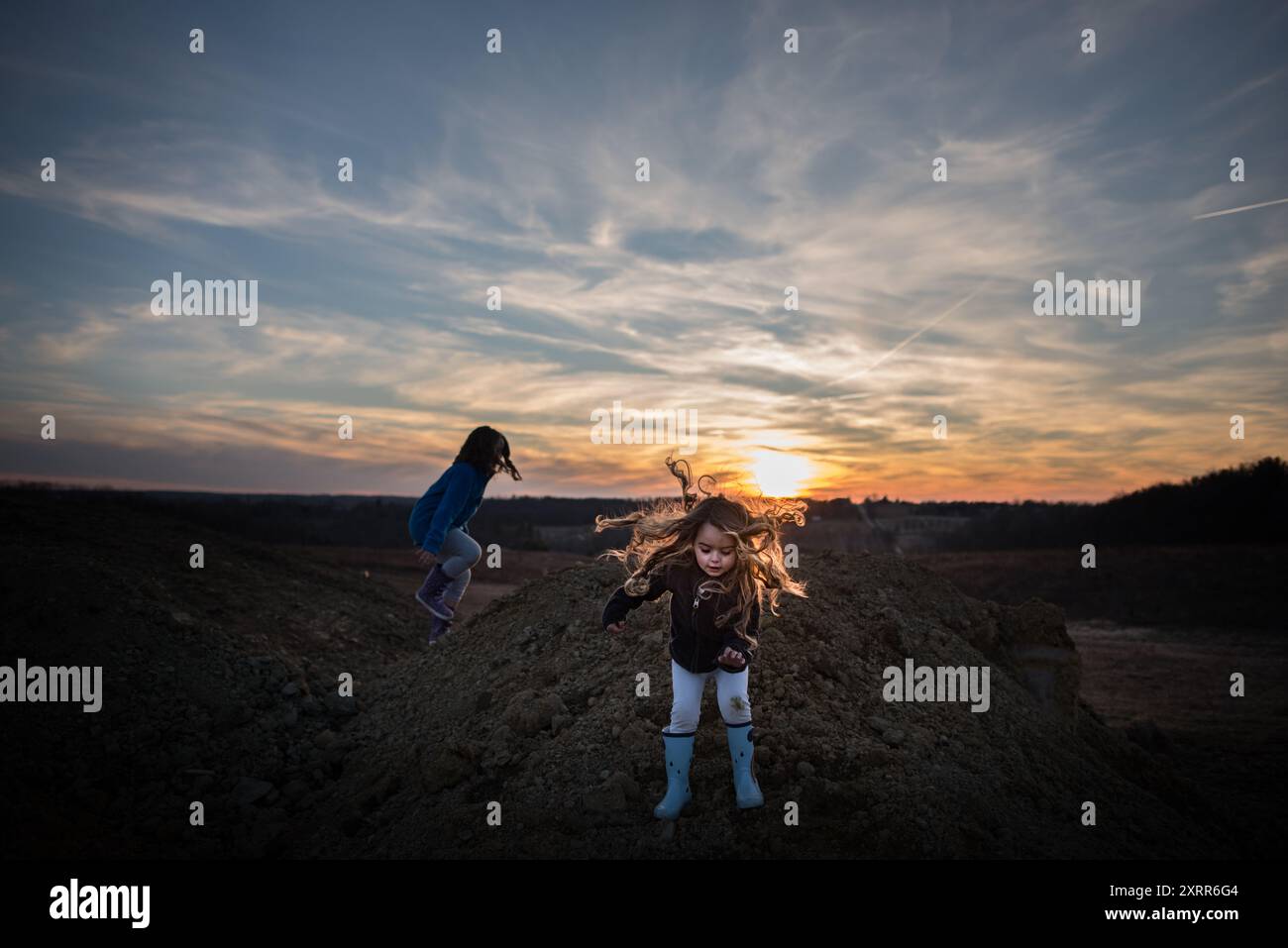 Junge Schwestern, die bei Sonnenuntergang auf Schotterhaufen spielen Stockfoto