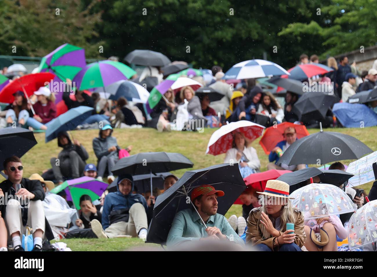 Zuschauer sitzen im Regen auf Henman Hill bei den Wimbledon Championships 2024 in London, England. Stockfoto