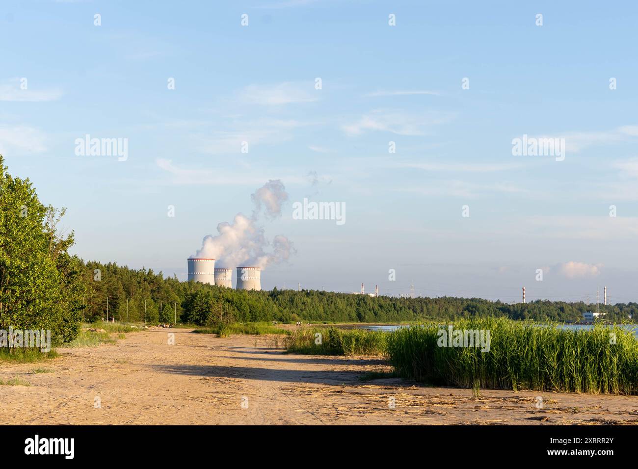 Blick auf einen Sandstrand und ein entferntes Atomkraftwerk mit Rauchwolken Stockfoto