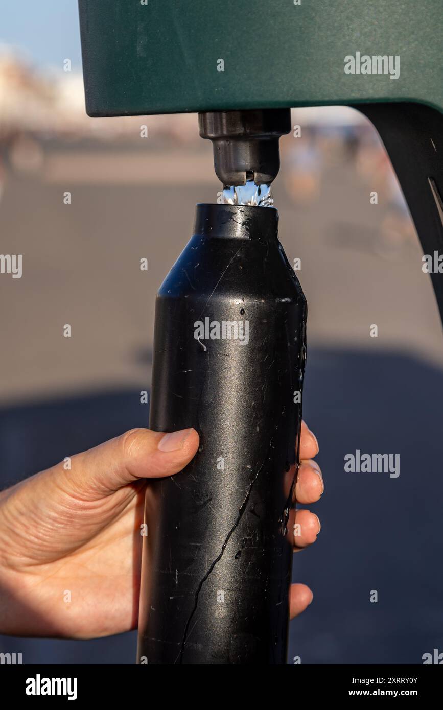 Eine Nahaufnahme einer wiederverwendbaren Wasserflasche, die an einem sonnigen Sommertag an einem Wasserhahn nachgefüllt wird Stockfoto