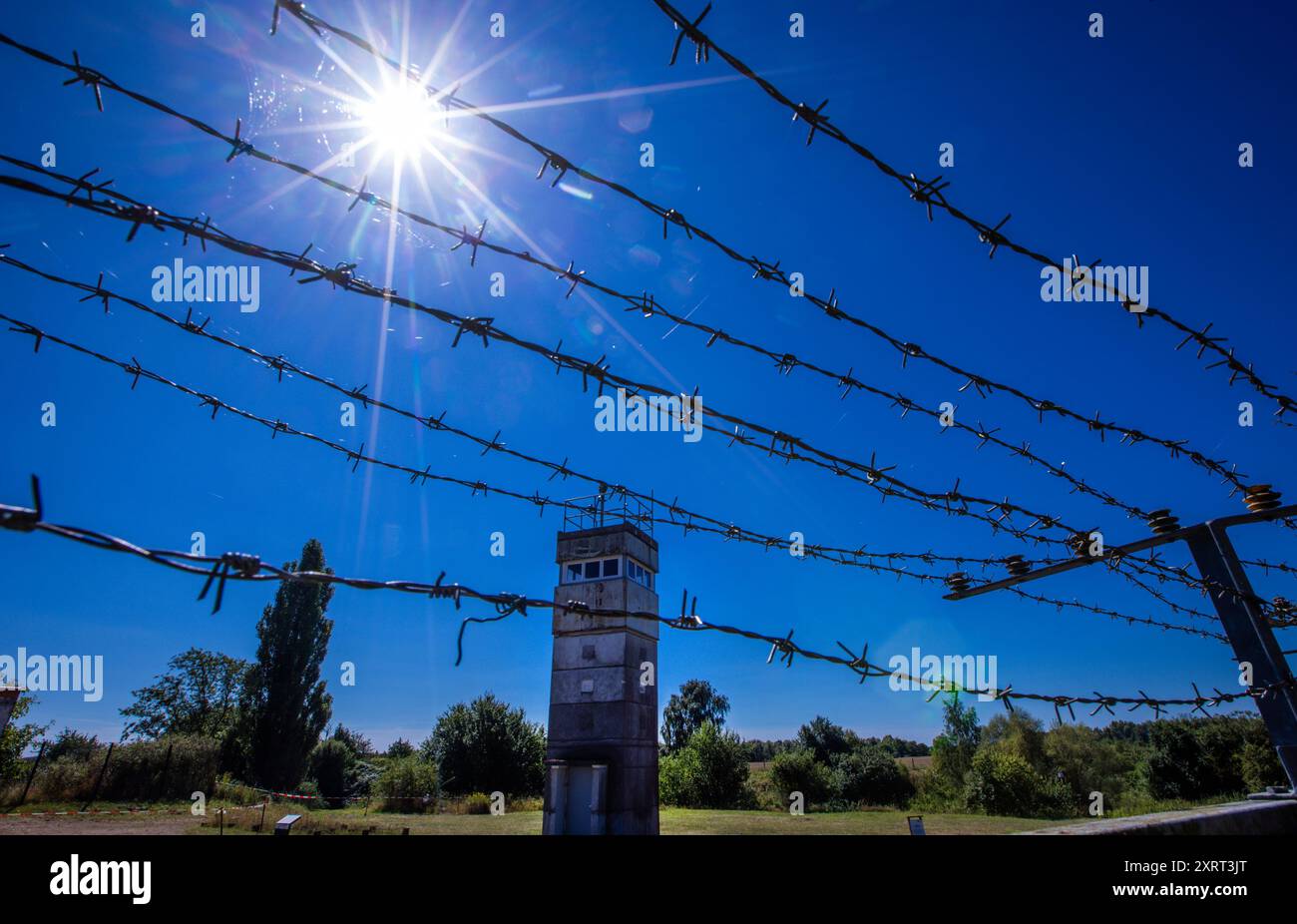 Schlagsdorf, Deutschland. August 2024. Ein Aussichtsturm der DDR-Grenztruppen aus den 1960er Jahren steht hinter einem Stacheldrahtzaun auf dem Gelände des Grenzhus Schlagsdorf. Zahlreiche Veranstaltungen erinnern an den Tag des Mauerbaus und der Schließung der innerdeutschen Grenze am 13. August 1961. Historiker schätzen, dass an der innerdeutschen Grenze rund 650 Menschen ums Leben kamen. Quelle: Jens Büttner/dpa/Alamy Live News Stockfoto