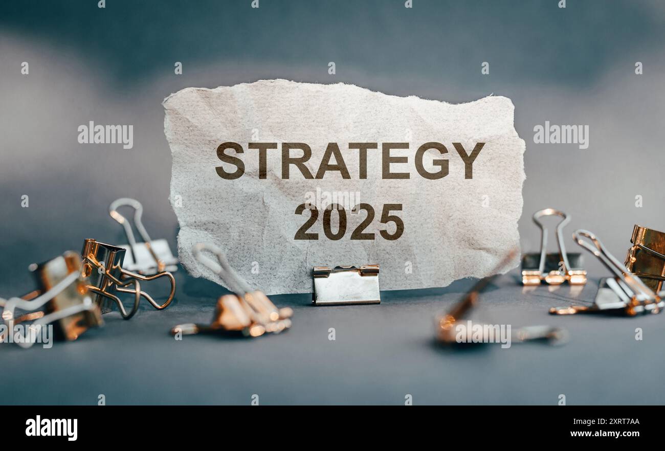 Auf einem zerrissenen Blatt Papier steht neben dem Jahr 2025 das Wort Strategie, umgeben von metallischen Binderklammern, die die Geschäftsplanung symbolisieren. Stockfoto