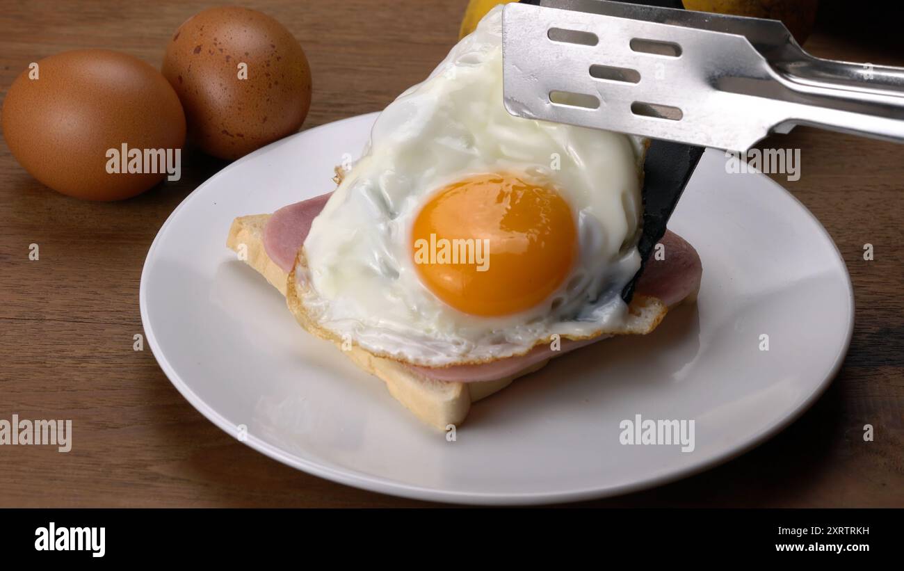 Legen Sie zum Frühstück einen Schinken und ein Spiegelei auf einen Toast in einer weißen Keramikschale. Stockfoto
