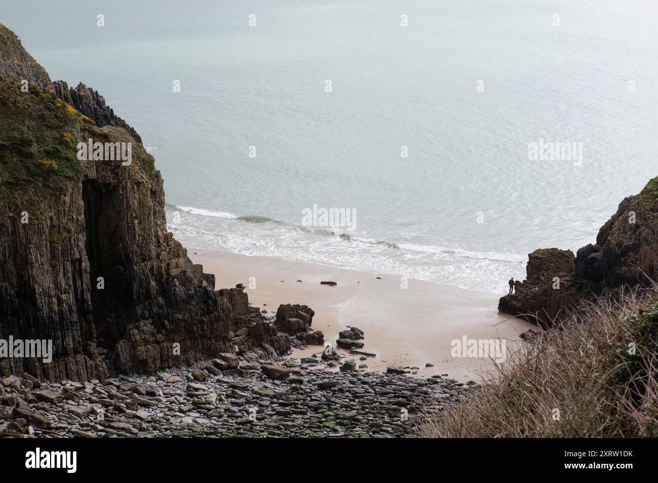 Blick hinunter auf einen kleinen Strand mit einer einzigen Figur, die auf Felsen in der Nähe des Meeres steht. Stockfoto