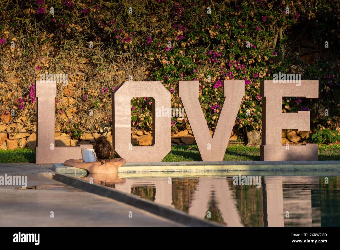 Sonnenbaden weibliche Lesebucher im Pool neben dem großen LIEBESSCHILD in Atzaro Stockfoto