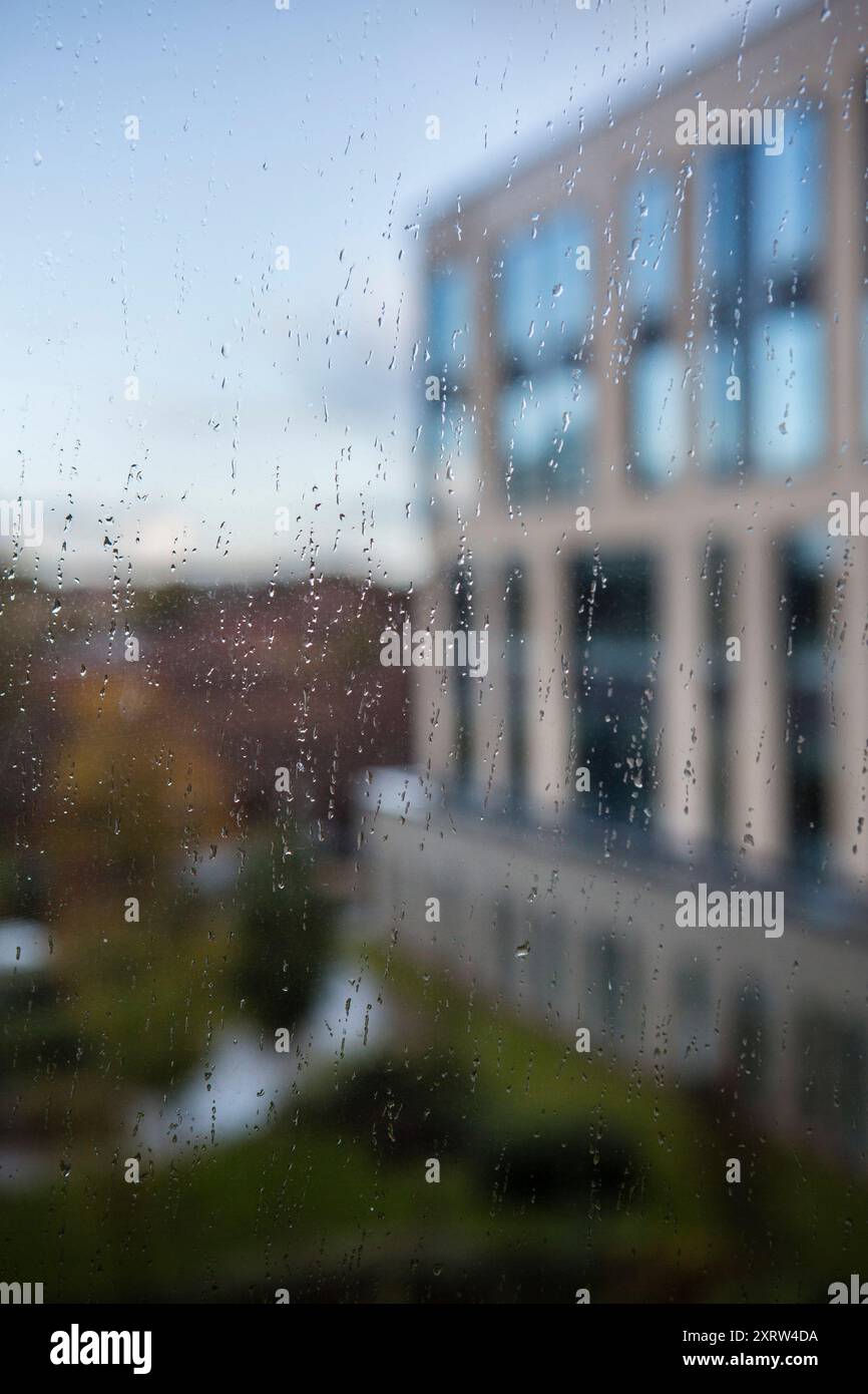 Blick durch ein Bürofenster auf die Gebäude draußen, während Regentropfen auf das Glas fallen. Stockfoto