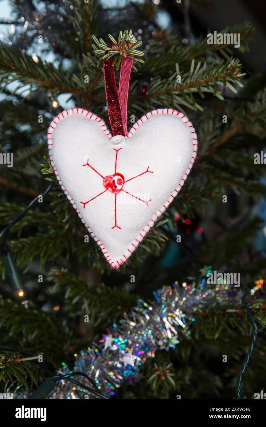 Eine herzförmige hausgemachte Dekoration und Lametta, die an einem weihnachtsbaum der Familie hängt. Stockfoto