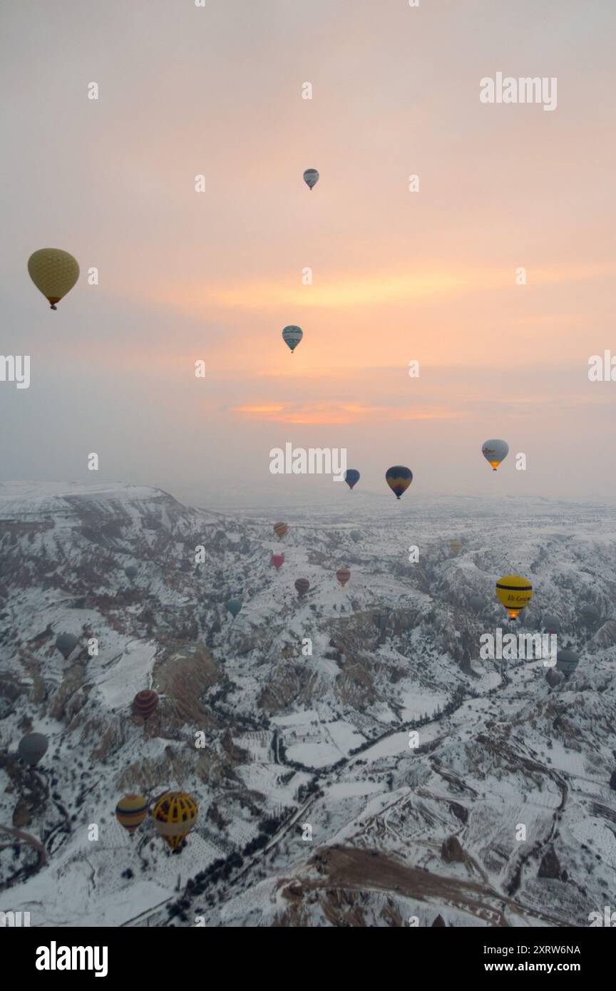 Heißluftballons treiben bei Sonnenaufgang über eine schneebedeckte Landschaft Kappadokiens und schaffen eine surreale und magische Winterszene Stockfoto