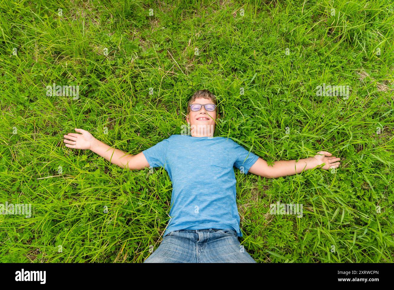 Das Kind entspannt sich auf grasbewachsenem Boden mit ausgestreckten Armen vor Freude. Stockfoto