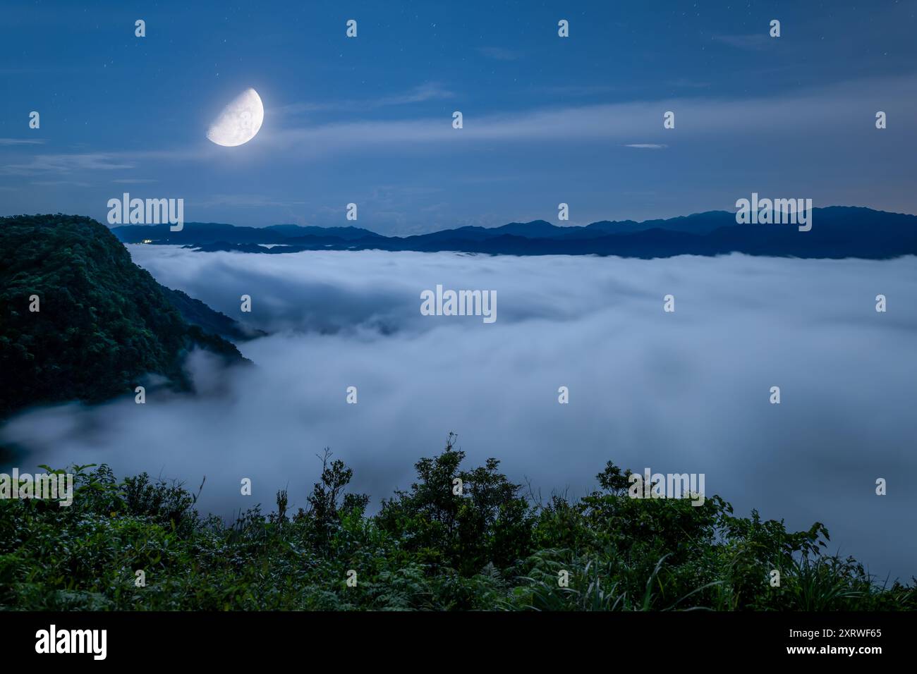 Eine ruhige Szene eines Vollmondes, der ein riesiges Wolkenmeer beleuchtet, das an Meereswellen erinnert. Der Himmel ist mit Sternen gespickt, was zu der ruhigen Atmosphäre beiträgt Stockfoto