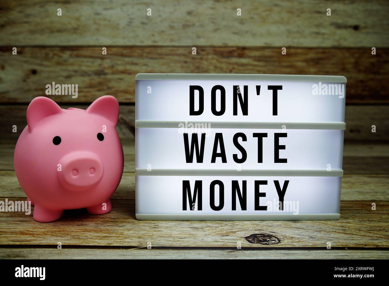 Vergeuden Sie keinen Geldtext auf LED-Leuchtkasten mit Sparen auf hölzernem Hintergrund, Geldkonzept Stockfoto