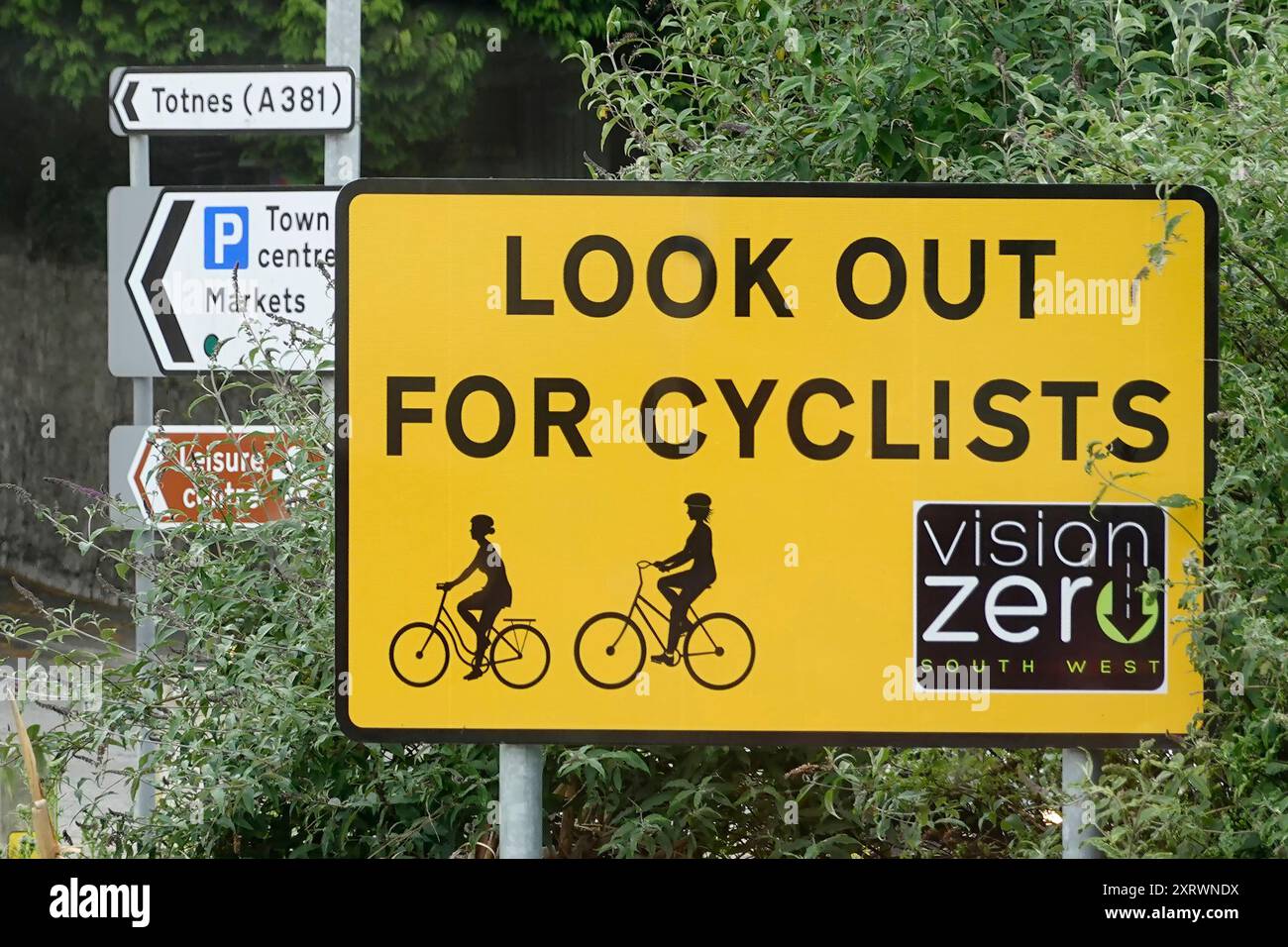 Halten Sie Ausschau nach Radfahrern. Ein deutliches gelbes Straßenschild an der Kreuzung des Kreisverkehrs ist ein multinationales Projekt der Vision Zero zur Verkehrssicherheit in England Großbritannien Stockfoto