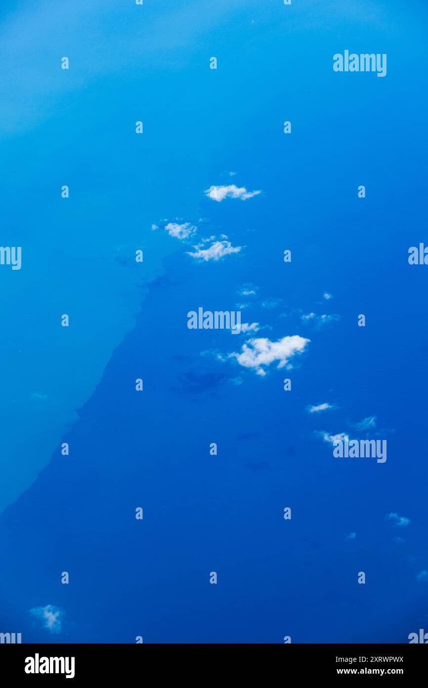 Winzige Wolken, die von einem Flugzeug weit unten gesehen werden, bilden ein tiefblaues Meer. Stockfoto