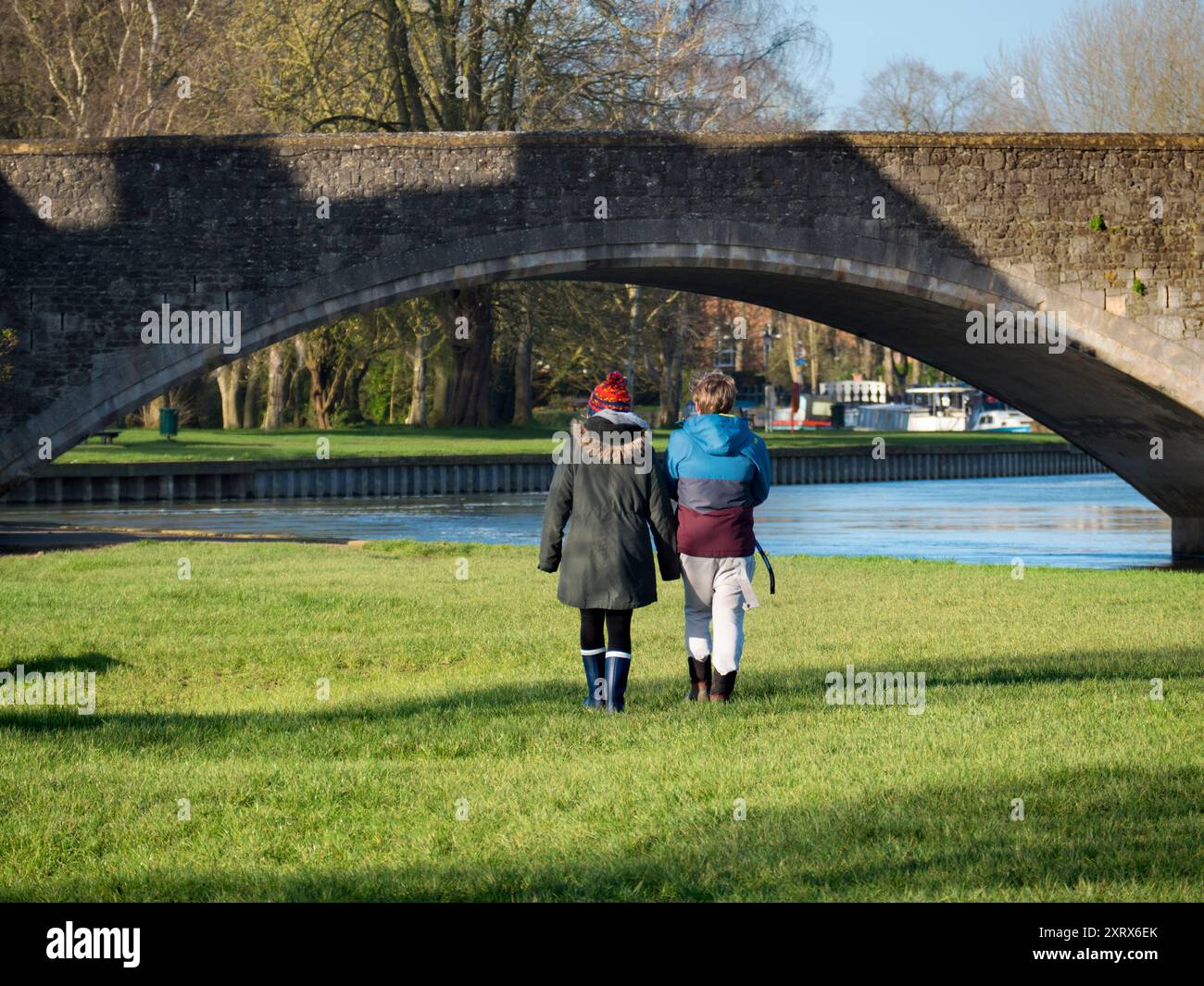 Abingdon behauptet, die älteste Stadt Englands zu sein. Dies ist die berühmte mittelalterliche Steinbrücke, die an einem schönen Sommermorgen zu sehen ist. Die Brücke wurde 1416 begonnen und 1422 mit lokalem Kalkstein fertiggestellt. Hier sehen wir ein umarmtes Paar, das bei Sonnenaufgang am Ufer der Themse in Richtung Brücke geht. Stockfoto