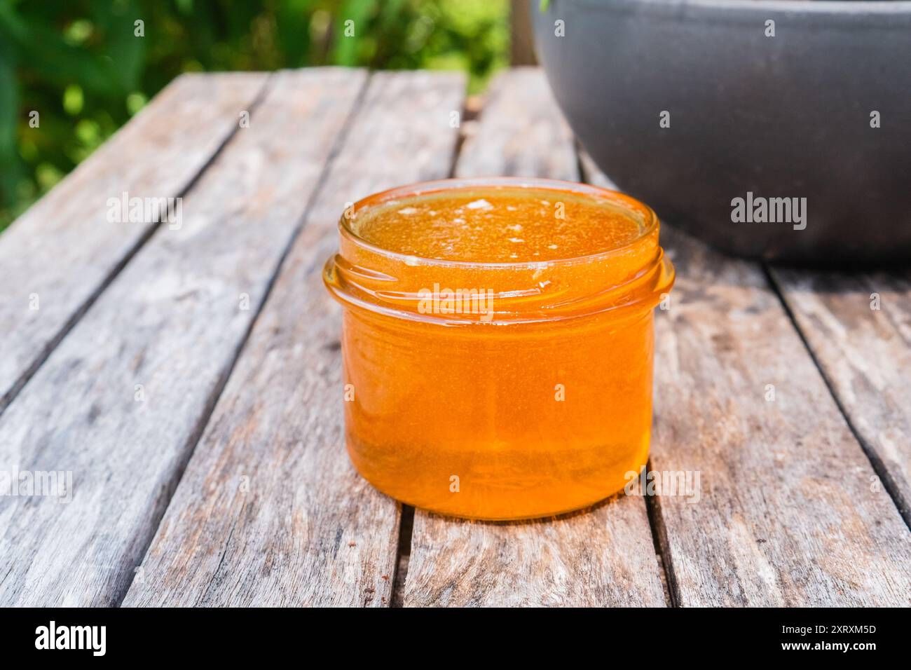 Honigglas gefüllt mit goldenem Honig, stehend auf einem Holztisch draußen in der Natur Stockfoto