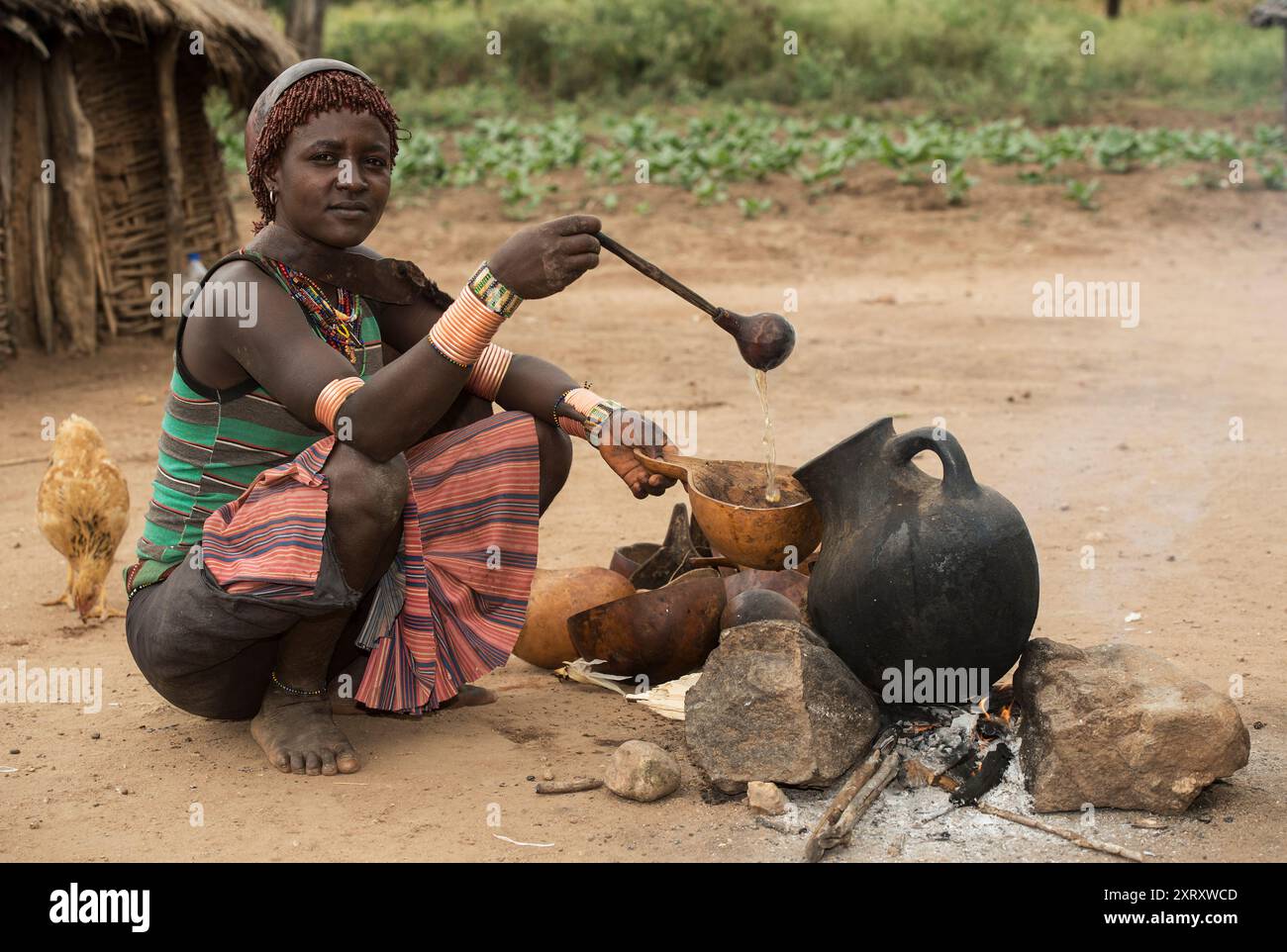 Eine junge Frau aus der Banna-ethnischen Gruppe gießt ein kaffeähnliches Getränk aus einer Tongefäß in eine Kürbisschale im südlichen Omo Valley, Äthiopien Stockfoto