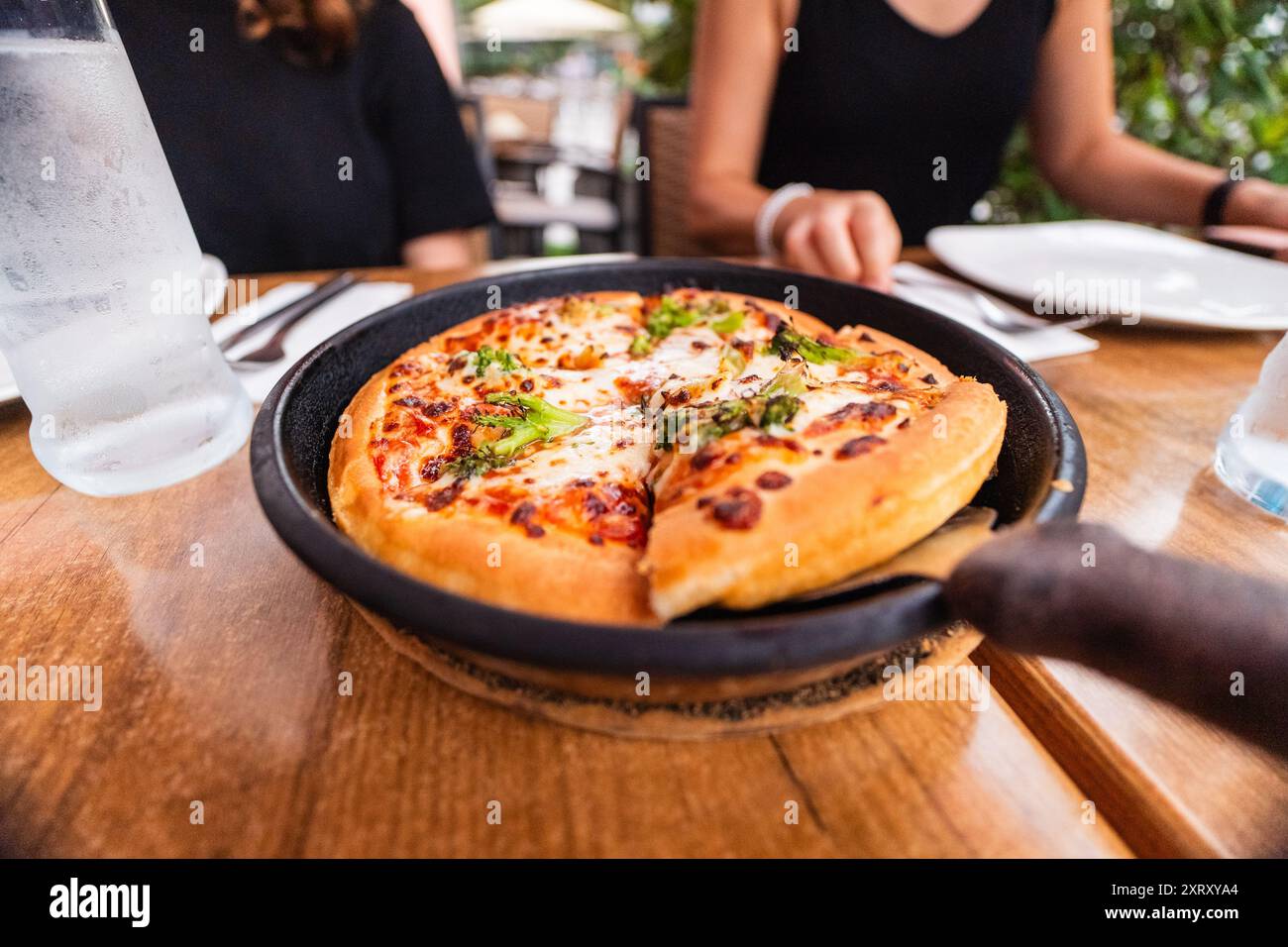 Vegetarische Brokkoli-Pizza in einer Bratpfanne mit Käse und gebackener Kruste, die in einem Restaurant ein Pizzastück aus der Pfanne pflückt Stockfoto