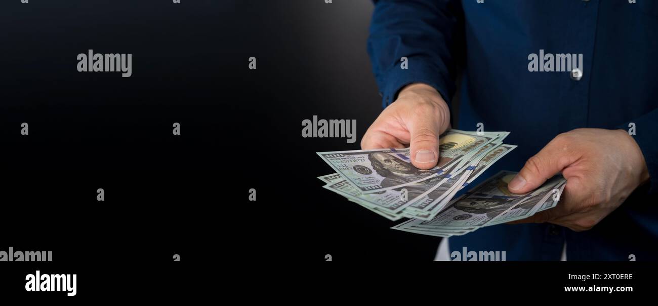 Hand gibt Geld isoliert auf schwarzem Hintergrund. Hände geben Geld in US-Dollar auf blauem Hintergrund Stockfoto