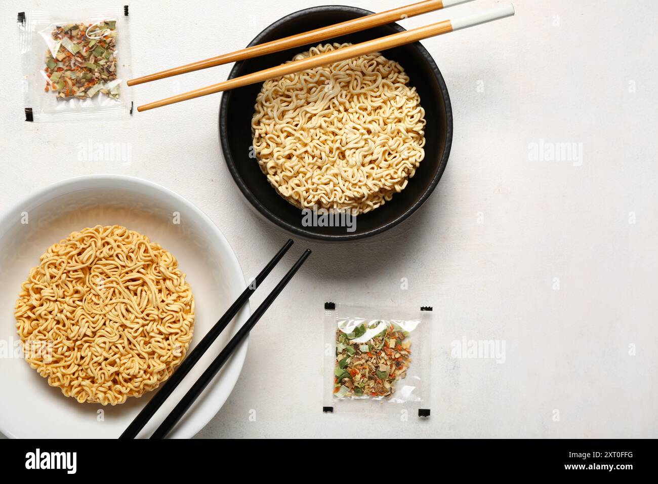Rohe Instantnudeln in Schüsseln mit Stäbchen und Gewürzen auf weißem Grunge-Hintergrund Stockfoto