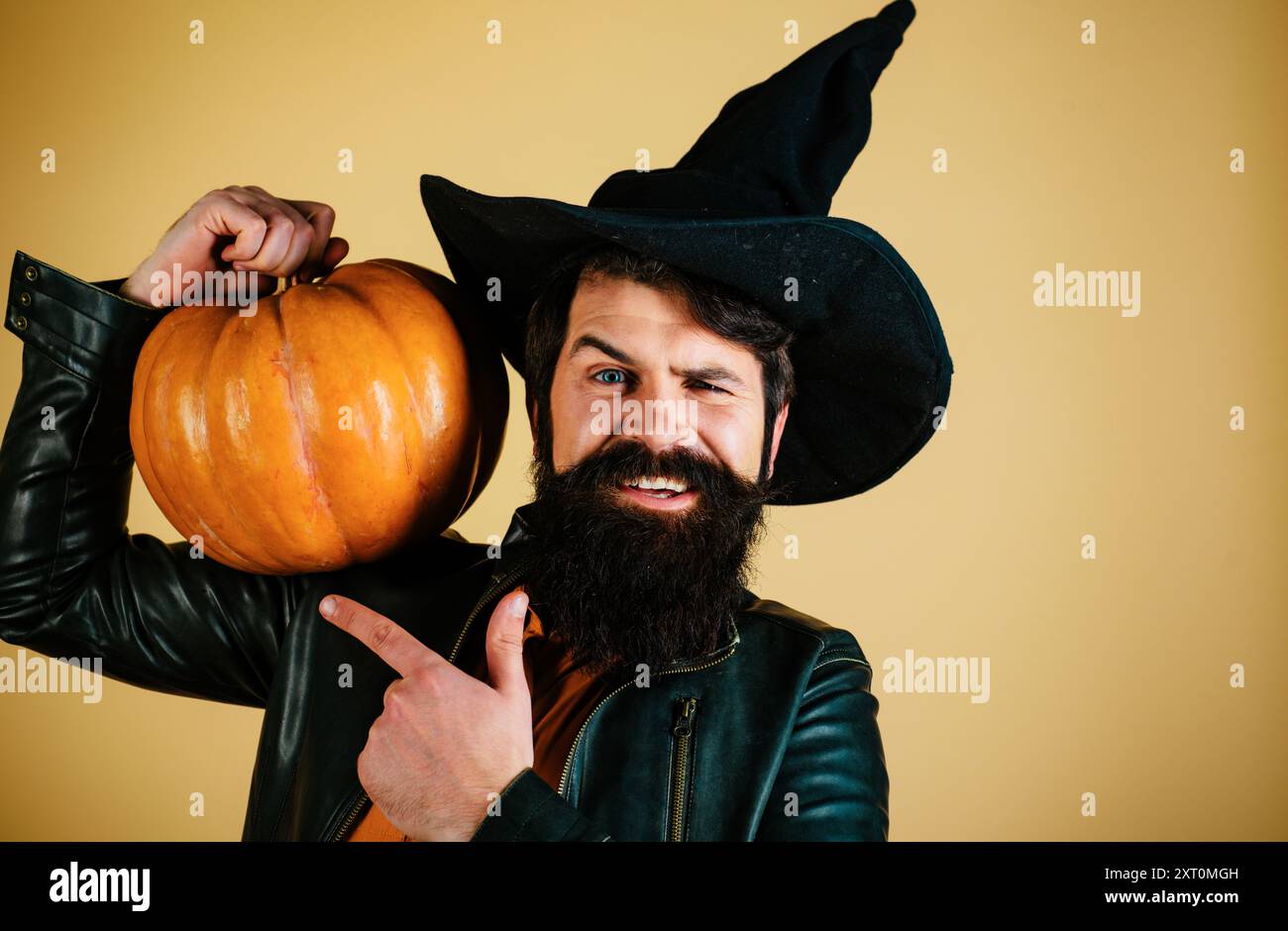 Porträt eines gutaussehenden Mannes mit Kürbis über isoliertem Hintergrund. Junger Mann mit Hexenhut, bereit für Halloween-Party. Thanksgiving saisonale Küche Stockfoto