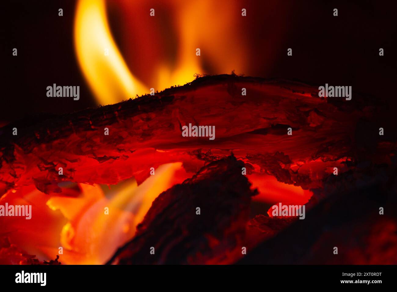 Helle orange Flammen um brennendes Holz im Dunkeln, Nahaufnahme Stockfoto