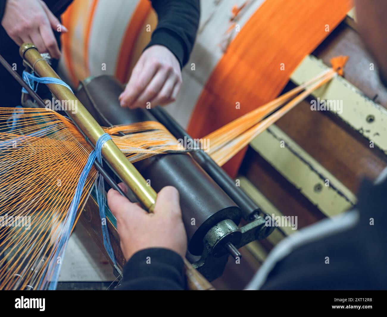 In einer Nahaufnahme werden die Hände und Maschinen der Garnverarbeitung in einer Textilfabrik erfasst, wobei der Schwerpunkt auf den lebhaften Fasersträngen liegt Stockfoto