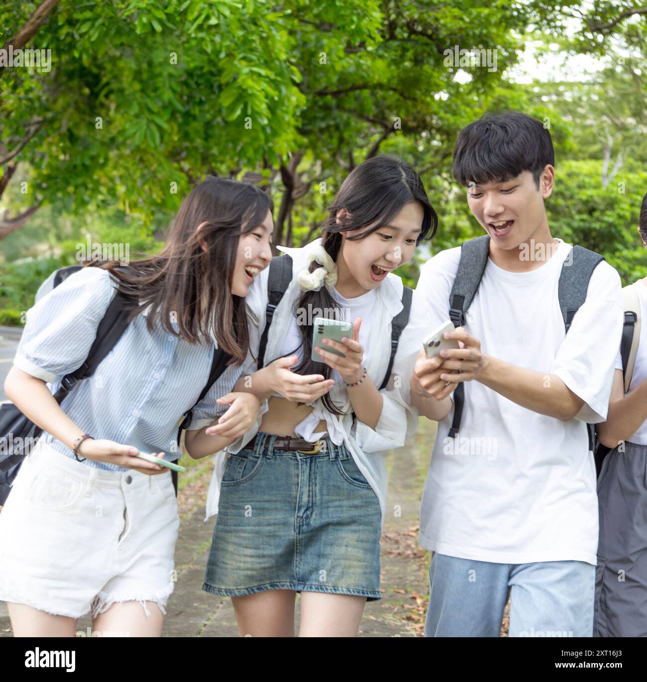 Glückliche Teenager, die Spaß haben, während sie ihr Mobiltelefon in der Schule benutzen Stockfoto