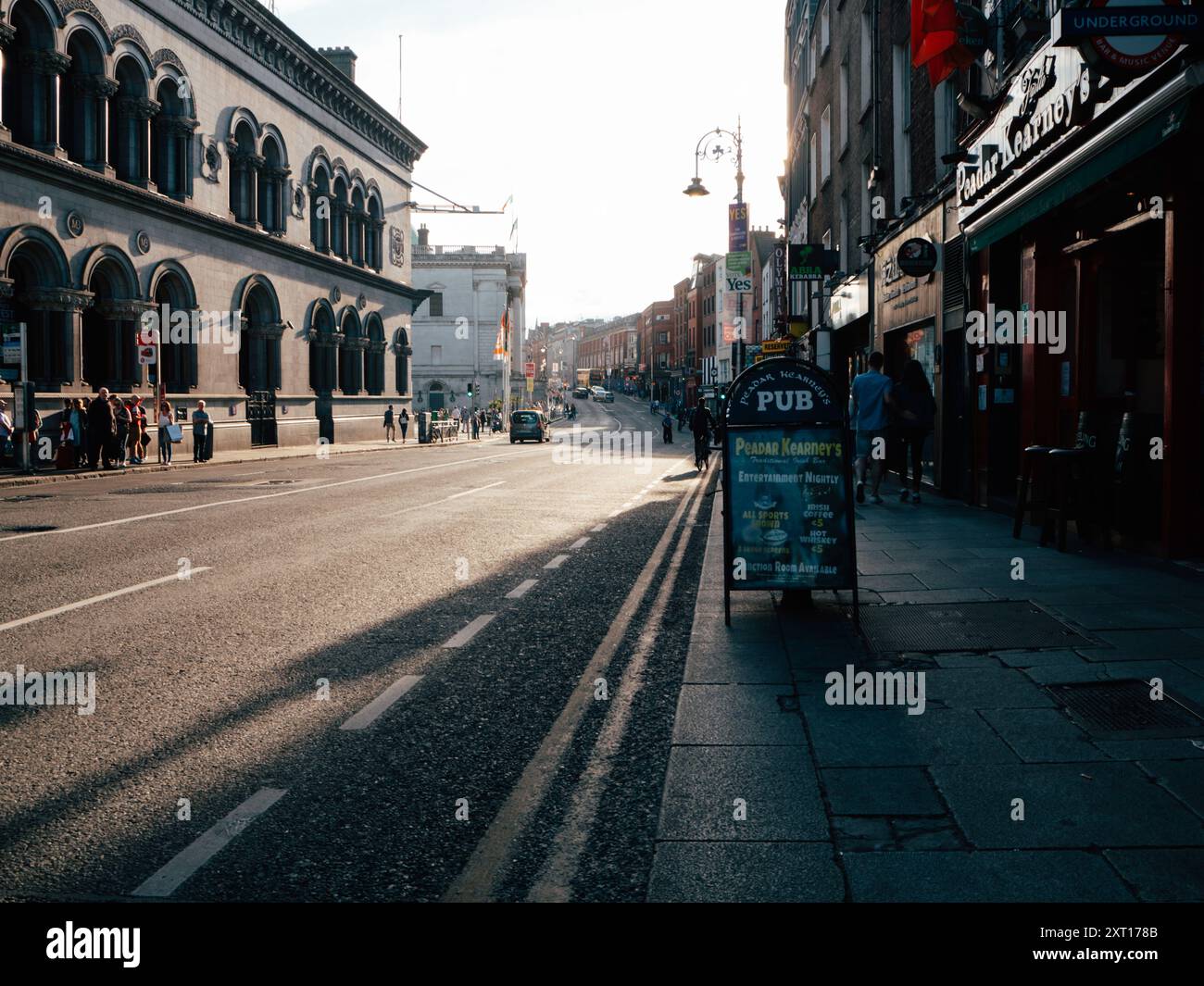 Das Licht am frühen Morgen taucht die ruhigen Straßen Dublins auf, während Fußgänger gemütlich spazieren gehen und Geschäfte beginnen, ihre Türen für den Tag zu öffnen. atmos Stockfoto