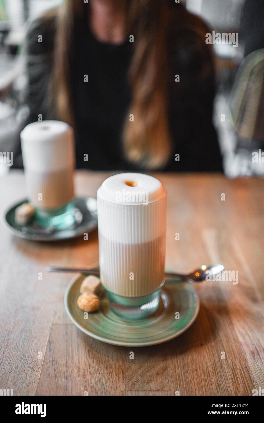 Köstlicher hellbrauner Latte Macchiato-Kaffee mit weichem Milchschaum in einem schönen gerippten Glas mit grünen Akzenten auf einer Platte mit Cookies auf einem Stockfoto