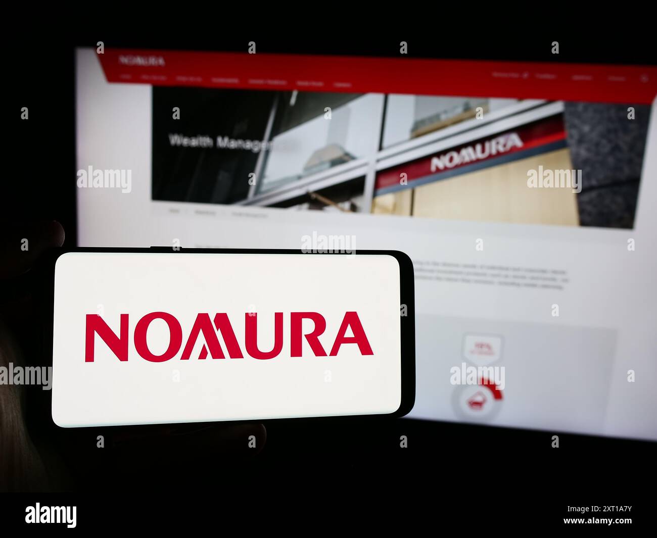 Person mit Smartphone und Logo des japanischen Finanzdienstleisters Nomura Holdings Inc. Vor der Website. Schwerpunkt auf dem Display des Telefons. Stockfoto