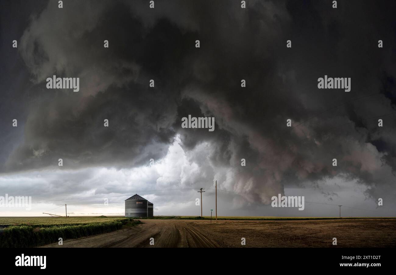 Unheilvolle Sturmwolken erheben sich über einer Landstraße mit einem einsamen Gebäude und einem Telefonmast, was auf ein bevorstehendes Unwetterereignis hindeutet. Joes, Colorad Stockfoto