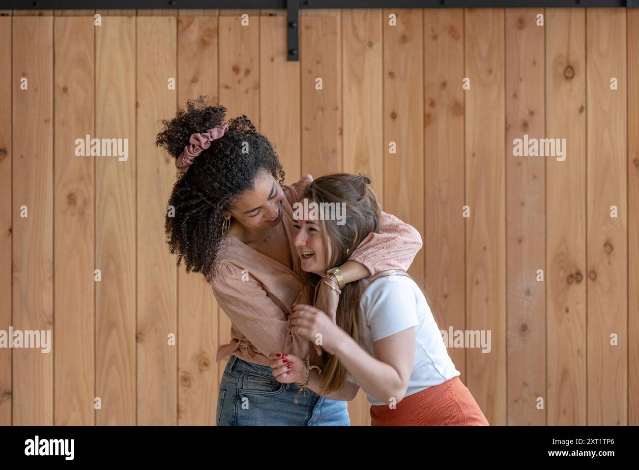 Zwei Frauen teilen sich eine fröhliche Umarmung in einem Raum mit Holzwänden. Panc05555 Copyright: XConnectxImagesx Stockfoto