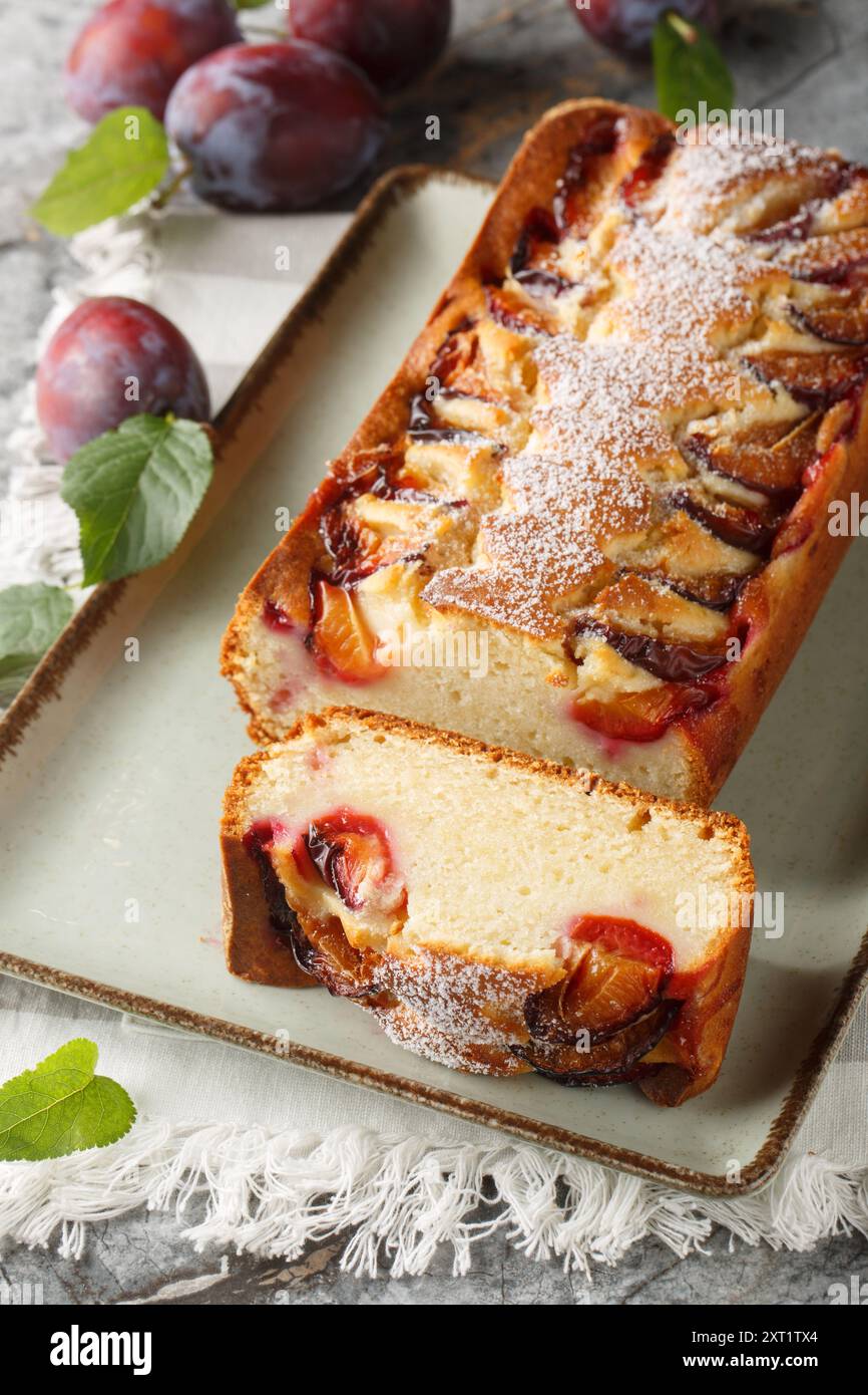 Zarter Biskuitkuchen mit Pflaumen und Joghurt in Nahaufnahme auf einem Teller auf dem Tisch. Vertikal Stockfoto
