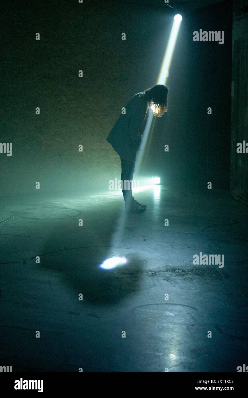 Ein einsamer Mensch steht gebadet in einem Lichtstrahl, mit gebeugtem Kopf, in einem verdunkelten Raum. Bola02627 Copyright: XConnectxImagesx Stockfoto