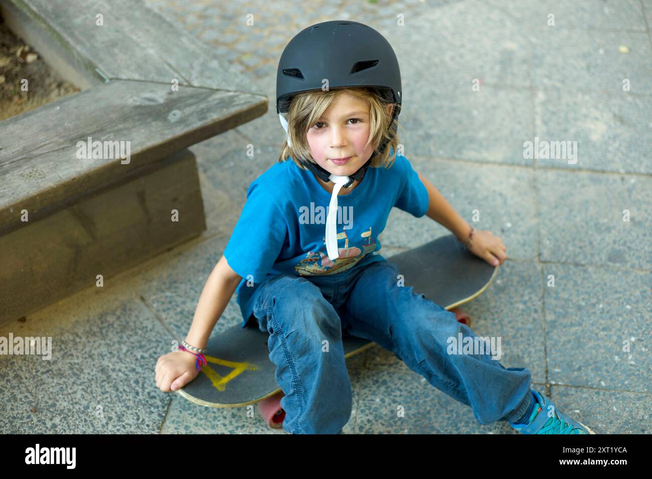 Ein kleines Kind in einem Helm sitzt selbstbewusst auf einem Skateboard und macht eine Pause auf den Trittstufen mit lässigem Look. Bola02719 Copyright: XConnectxIma Stockfoto