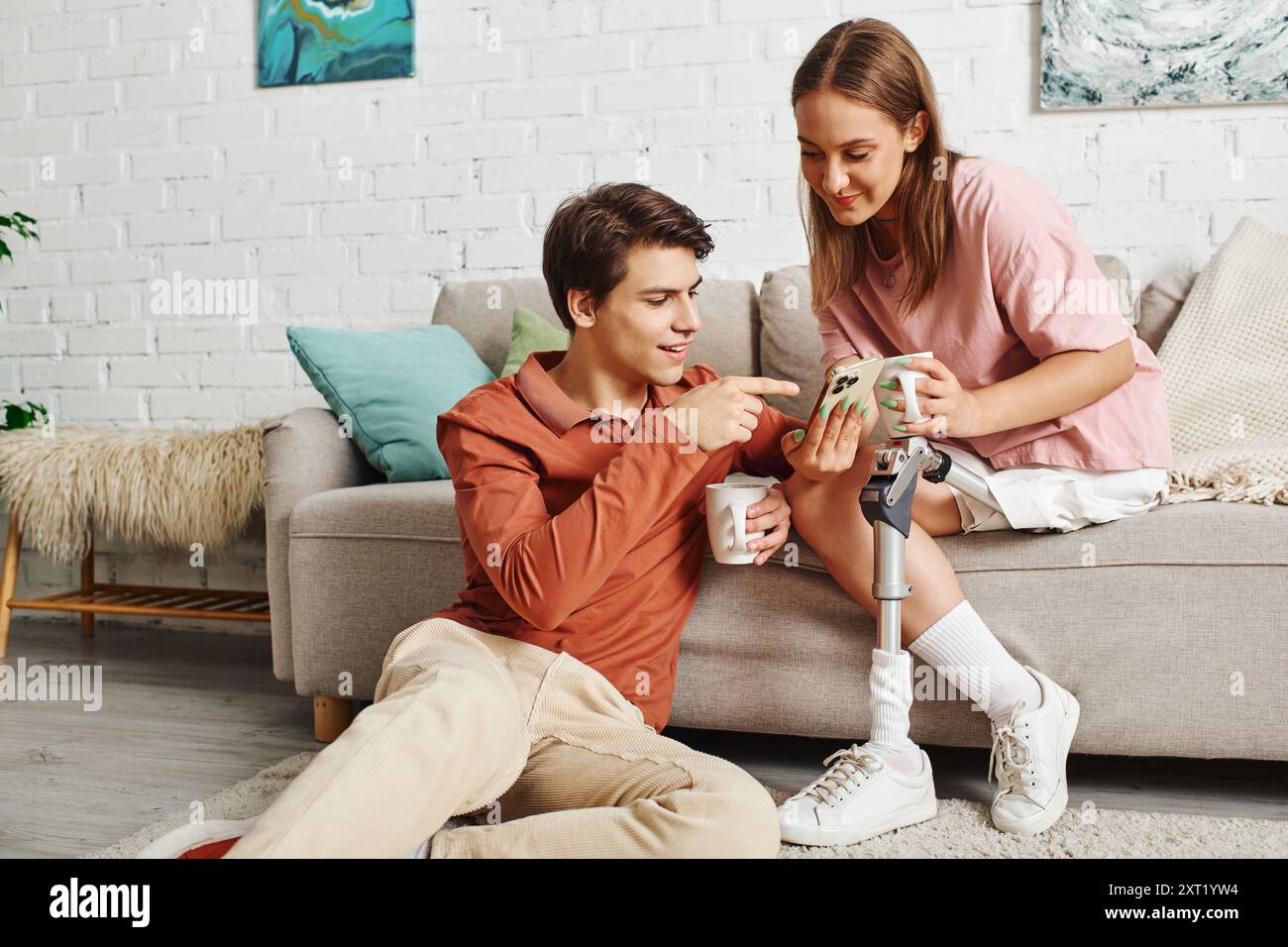 Eine Frau mit einer Beinprothese und ihr Freund genießen gemeinsam eine Tasse Kaffee in ihrem Wohnzimmer. Stockfoto