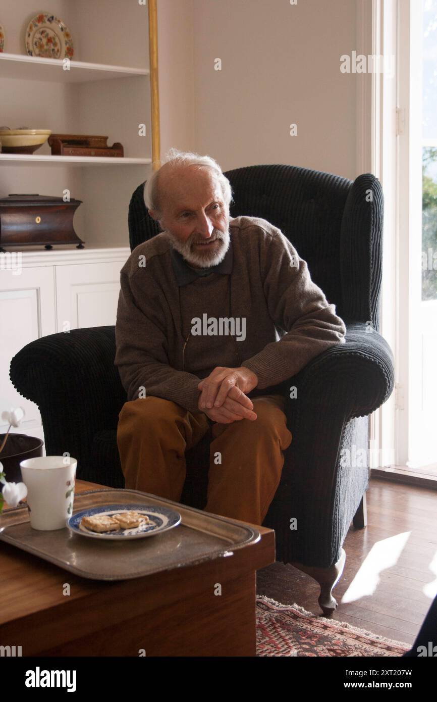 Älterer Mann sitzt in einem gemütlichen Wohnzimmerstuhl neben einem Couchtisch mit einem Teller Plätzchen Auckland Neuseeland evpe00718 Copyright: XConnectxImage Stockfoto