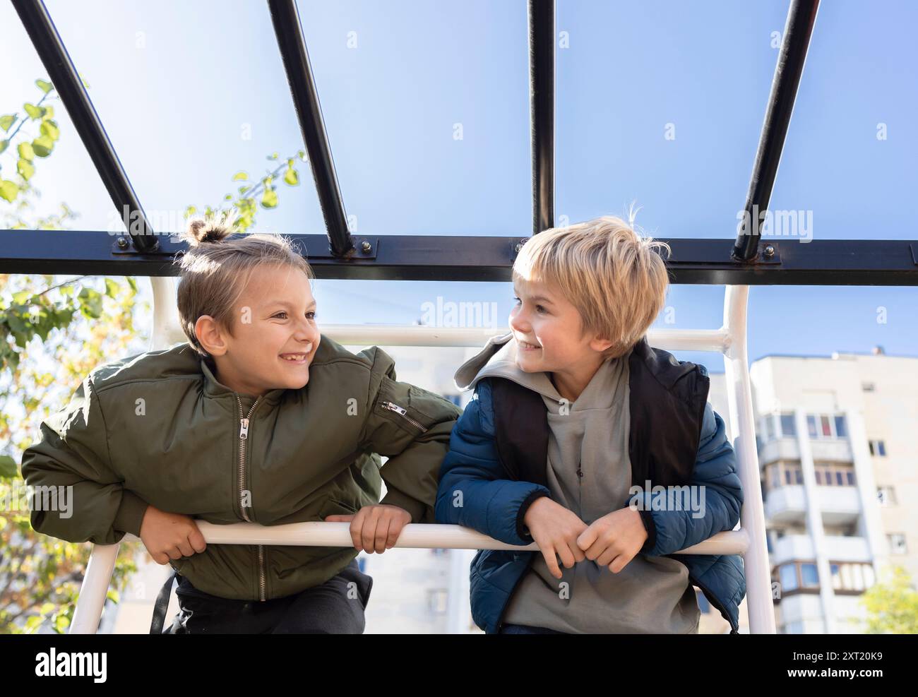 Zwei 7-8-jährige Freunde unterhalten sich auf dem Spielplatz an einem sonnigen Frühlings- oder Herbsttag. Schaut sich an. Joy Meeting. Kindheit Stockfoto