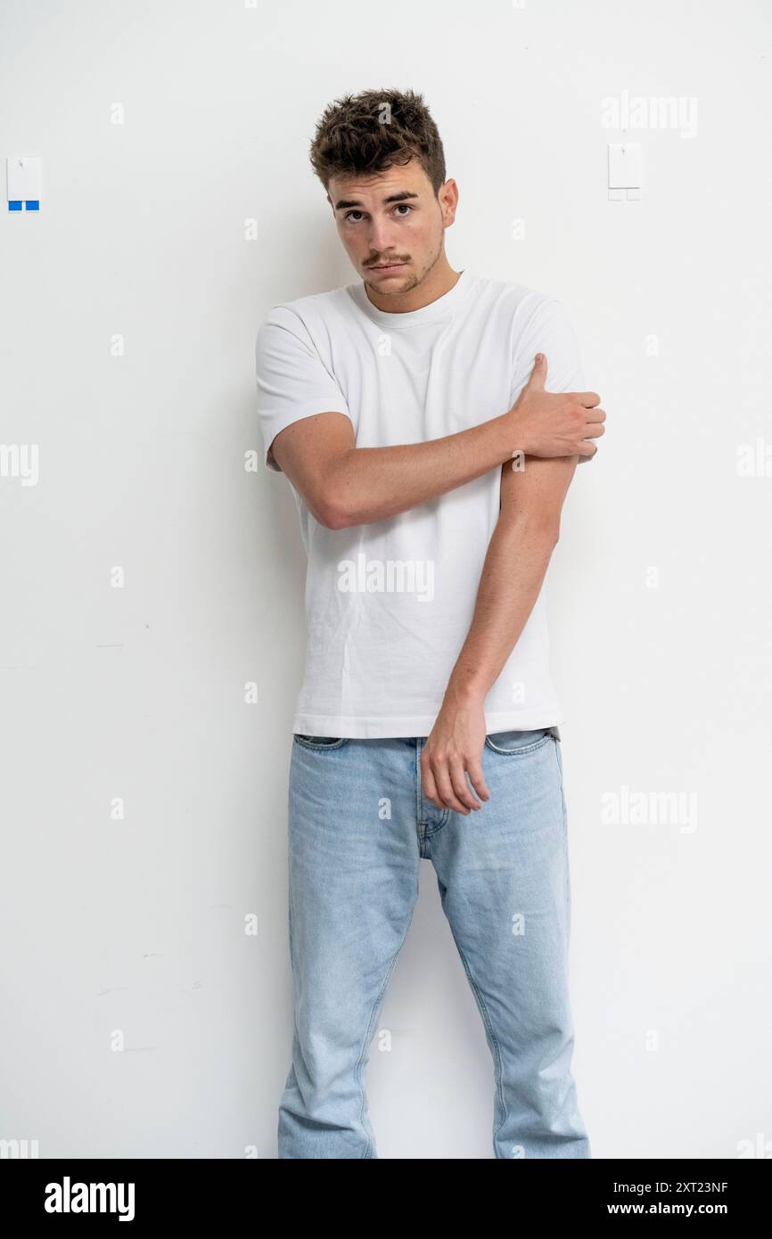 Junger Mann, der sich an eine weiße Wand lehnt, mit gekreuzten Armen und einem kontemplativen Ausdruck. Panc06074 Copyright: XConnectxImagesx Stockfoto