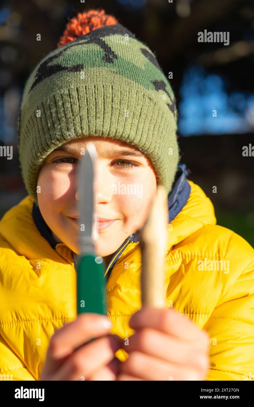 Der Entdecker zeigt sein Messer und den Stock, den er geschärft hat, in einer Überlebenswerkstatt für Kinder in der Natur Stockfoto