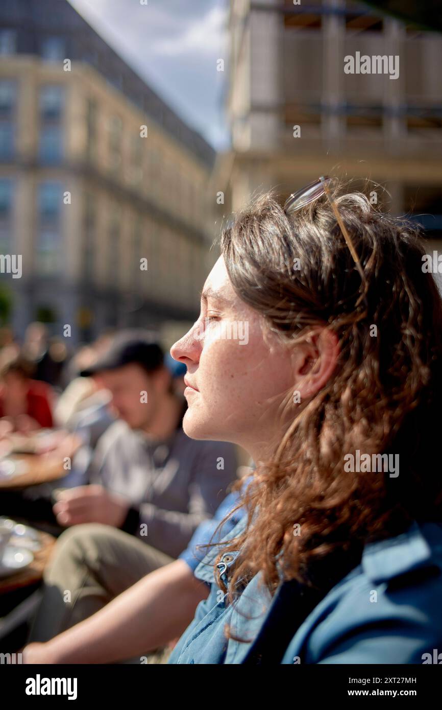 Eine Frau mit lockigen Haaren genießt den Sonnenschein auf einer Stadtstraße und sieht nachdenklich aus, während das Sonnenlicht ihr Profil unterstreicht. Bola02794 Copyright: XCO Stockfoto