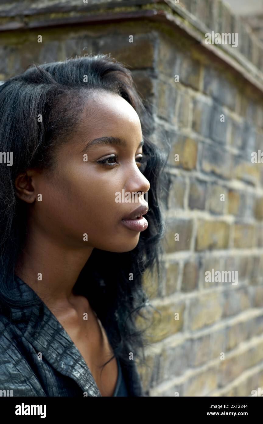 Seitenprofil einer jungen Frau mit kontemplativem Ausdruck vor Backsteinmauerhintergrund. Bola02858 Copyright: XConnectxImagesx Stockfoto