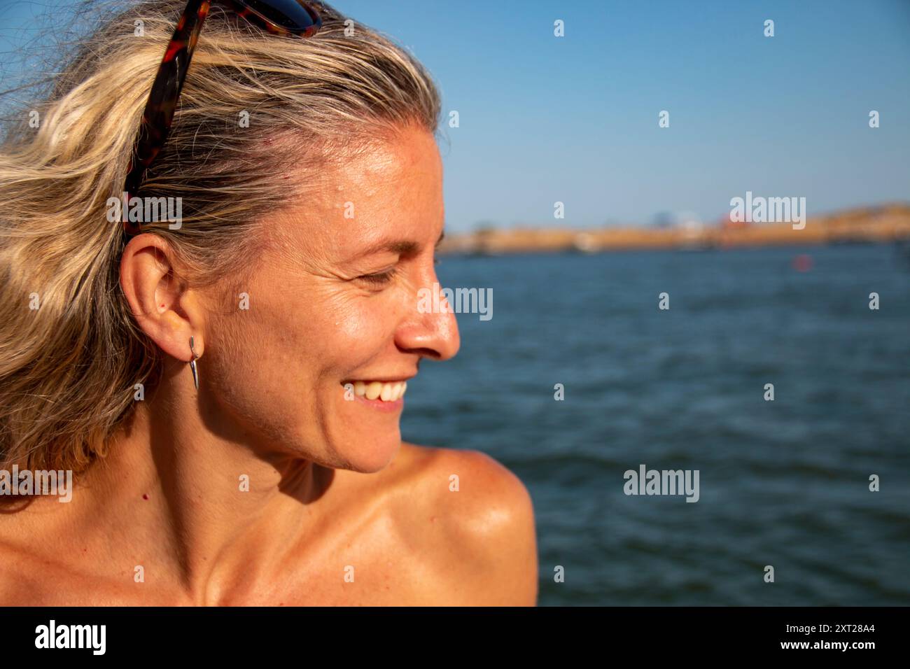 Blonde Frau mit lockeren Haaren und Sonnenbrille beugt sich über die Seite eines Bootes über die Wellen und das blaue Meer Stockfoto