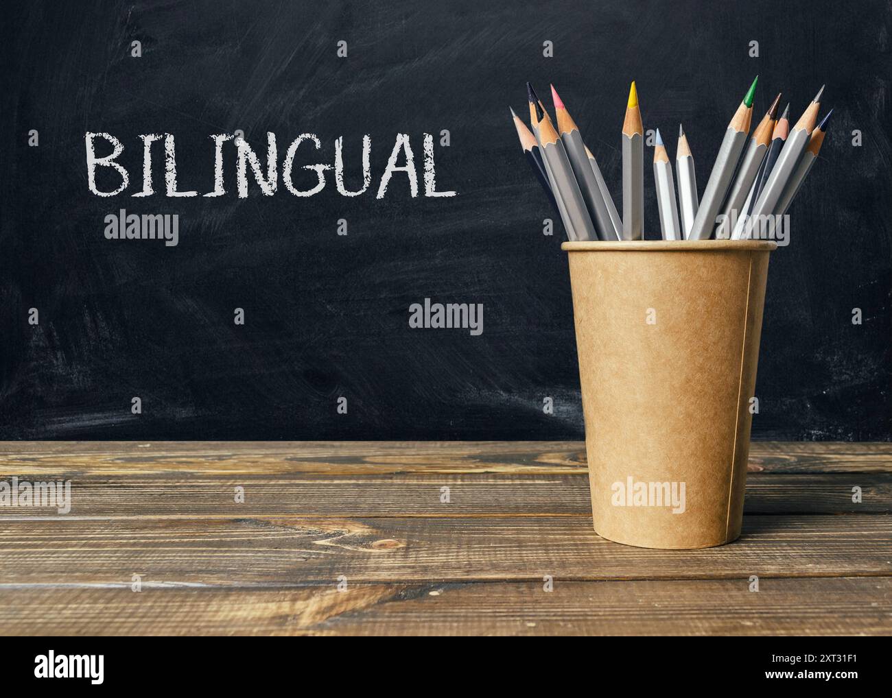 Ein Holztisch mit einer braunen Tasse und einem Haufen Bleistifte. Auf dem Becher steht das Wort zweisprachig Stockfoto
