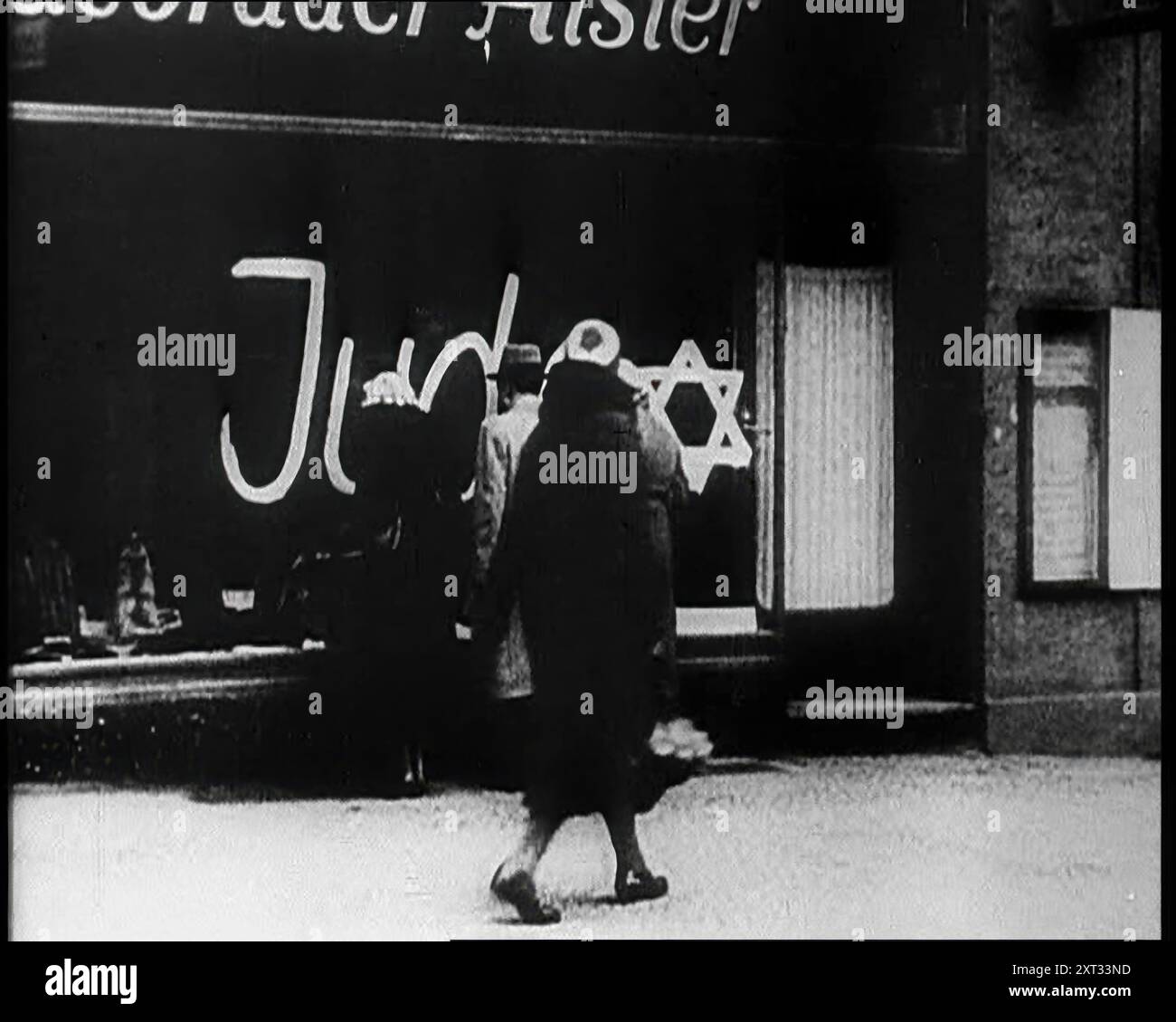 Zivilisten, die auf das Schaufenster schauen, mit Graffiti-Aufschrift: "Juden", 1933. "Wieder einmal, in der langen Geschichte der Welt, Qualen für die Juden". Aus „Time to Remember – The Time of the Monster“, 1933 (Reel 4); ein Dokumentarfilm über die Ereignisse von 1933, Rise of Roosevelt und Hitler. Stockfoto