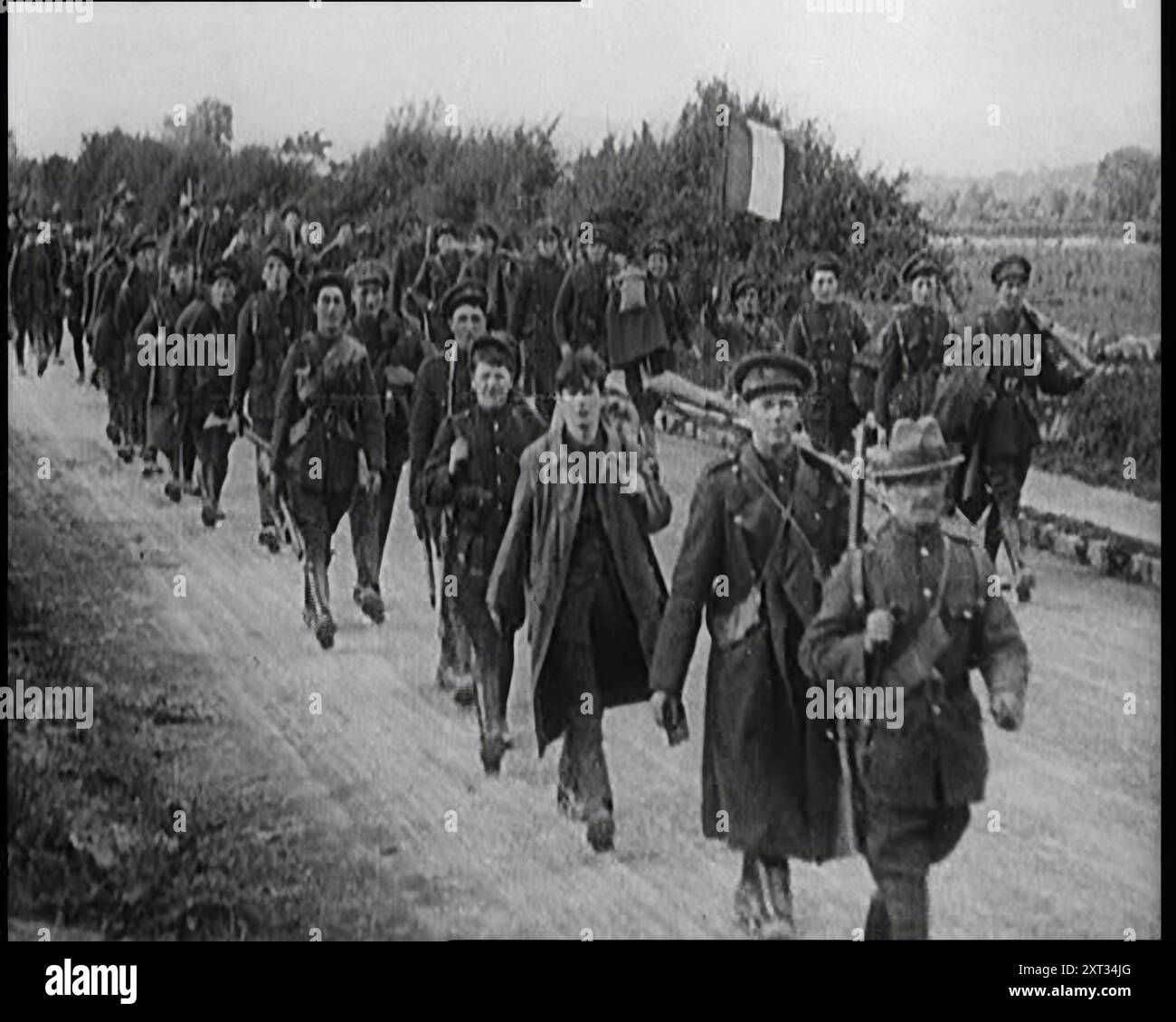 Irische Freistaat-Soldaten marschieren entlang einer Straße, 1922. "Nach Jahren des Blutvergießens wurde ein vertrag unterzeichnet, und in Dublin ersetzte eine neue Flagge den Unions-Jack. Irland, mit Ausnahme der sechs Grafschaften von Ulster, war zum irischen Freistaat geworden. Der Freistaat bildete sogleich seine eigene Armee, Tausende stürmten sich, um sich zu engagieren. Es war patriotisch und es war ein Job... Enthusiasmus machte den anfänglichen Mangel an Ausrüstung wieder wett. Und es war etwas ironisch, dass diese ersten Soldaten eines freien Irlands britische Khaki trugen, grün gefärbt. Südirien war frei, und Irland freute sich." Aus "Zeit zum erinnern - still sitzen und G Stockfoto