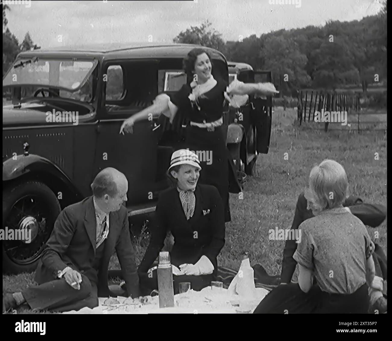 Männliche und weibliche Zivilisten beim Picknick neben einem Auto, 1931. „Dem ganzen entfliehen zu können, war... ein weiteres Merkmal der Zeit. Mit dem Auto, in die Pedale oder zu Fuß suchten die Massen die frische Luft, so als ob auch das gerade erfunden worden wäre." Aus „Time to Remember – A New Era“, 1931 (Reel 2); Dokumentarfilm über die Welt in den frühen 1930er Jahren Stockfoto