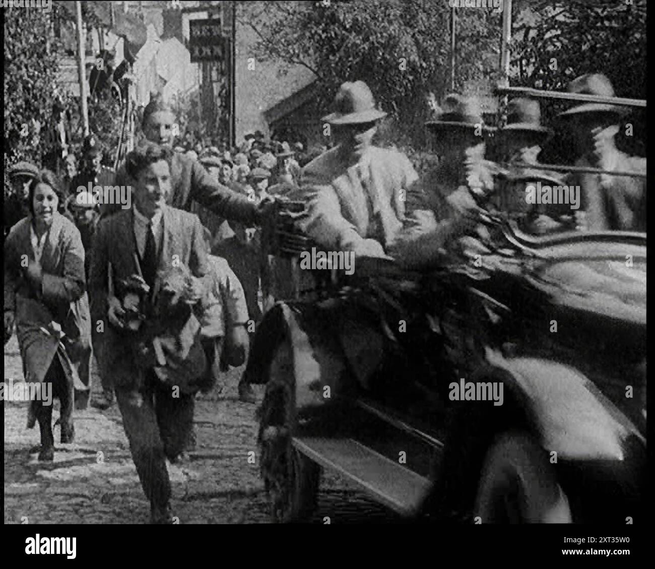 Die Menge jagt einem Auto, während er eine Hügel kopfsteingepflasterte Straße hinaufklettert, 1920. „Für diejenigen mit mechanischem Biegen bot 1920 viele neue Möglichkeiten. Die Hügel Großbritanniens hinauf und hinunter fuhren Autos und Motorräder. Rallyes, Rennen und Tests standen nun auf allen Sportkalendern... für die Verbrennungsbegeisterten sah die Straße vor uns interessant aus.“ Aus "Time to Remember - the Plunge into Peace", 1920 (Reel 4); Ereignisse von 1920 - Hochzeiten, Frauenrechte, industrielle Unruhen und Probleme in Irland Stockfoto