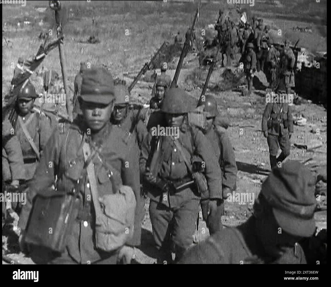 Männliche japanische Soldaten mit Gewehren, die einen Hügel hinauflaufen, in der Nähe der Stadt Hankow, 1937. Japanische Invasion Chinas. Vor Hankow donnern die japanischen Geschütze in die alten Befestigungsanlagen. Die Vergangenheit geht vor einer neuen und schrecklichen Vorstellung von der Zukunft ein. Die Vorstellung, dass die Macht Recht hat, und die Erde wird von den Starken geerbt werden... mit dem Fall Hankows huldigen die Eroberer den Glauben, der sie zu ihren Kriegen trieb. Aus "Time to Remember - Sense of Values", 1937 (Reel 4); Dokumentarfilm über die Ereignisse von 1937, Krieg im Fernen Osten, Aufbau bis zum Krieg Stockfoto